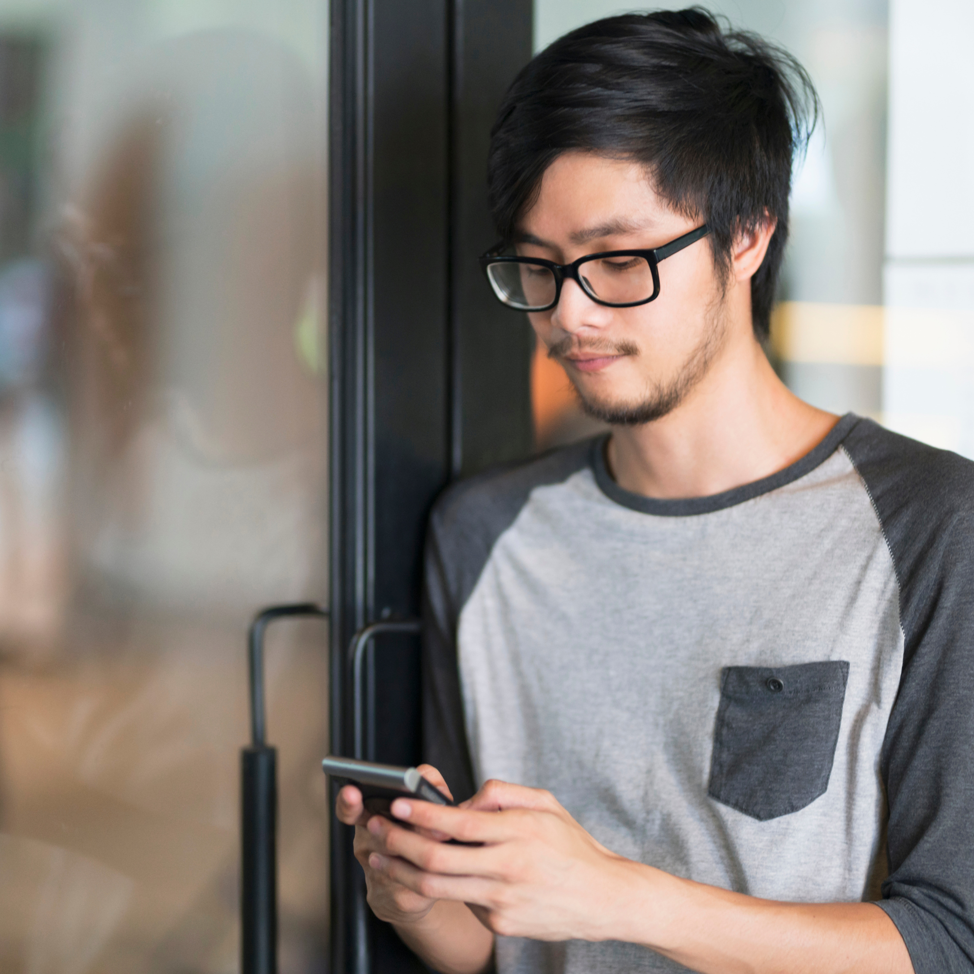 Junger Mann mit Brille schaut ruhig auf sein Smartphone